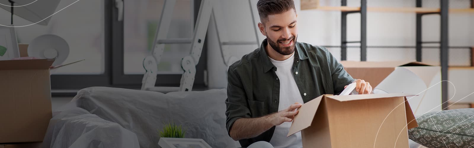 Rapaz abrindo uma caixa de papelão dentro da sua casa nova comprada pelo consórcio Embracon