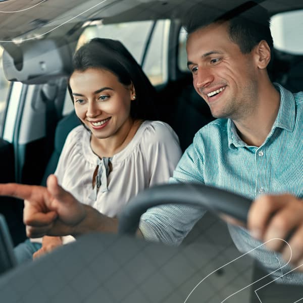 Simule o seu consórcio de carros e comece a investir no seu futuro agora mesmo! Casal sorrindo dentro do carro enquanto o homem segura o volante e toca no painel
