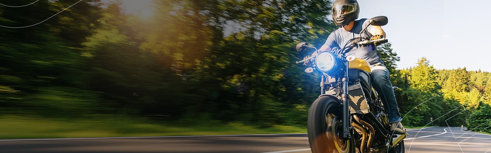 O Consórcio de Motos Embracon é o jeito mais rápido e seguro para você conquistar a sua moto sem juros e sem entrada Pessoa pilotando uma moto velozmente pela estrada cercada de árvores em um dia ensolarado