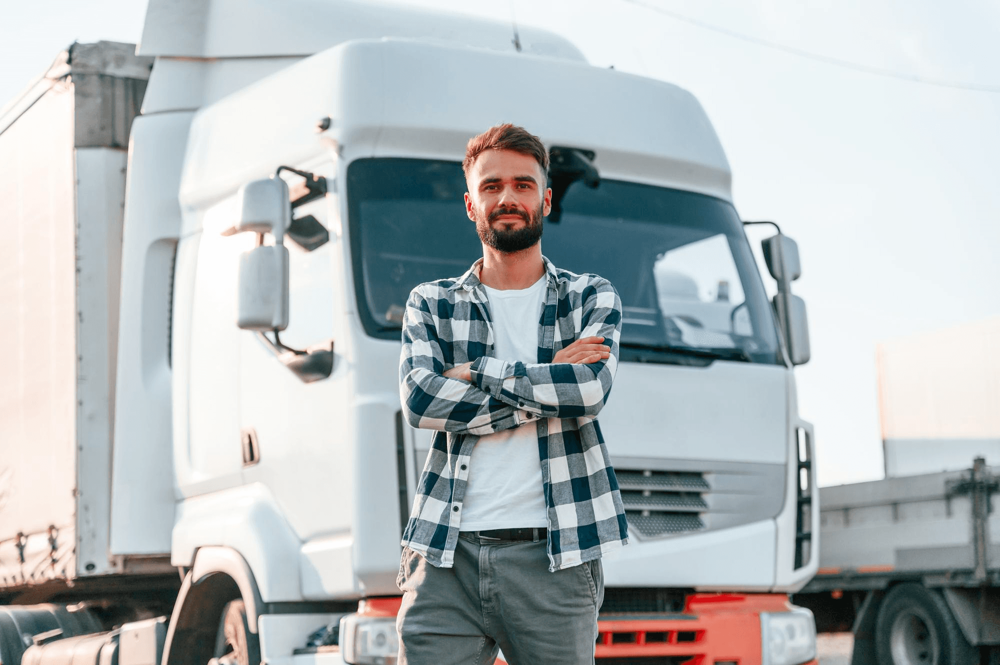 O futuro da sua empresa está nas suas mãos com o consórcio de pesados Embracon. Simule agora! Homem de braços cruzados em frente a um caminhão branco adquirido pelo consórcio de veículos pesados Embracon